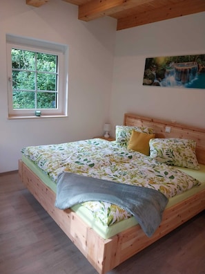 Una cama de madera con ropa de cama floral, una ventana con vistas a la vegetación y un cuadro de una cascada en la pared.