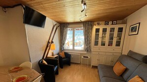A cozy living room with a dining table set, a sofa, a cabinet with glass doors, and a television mounted on the wall. - Ski-In/Ski-Out Studio at Les Gets, Close to Village Center (Les Gets)