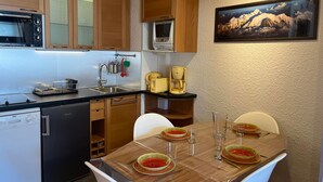 A compact kitchen with wooden cabinets, a microwave, a coffee maker, and a dining table set for two with plates and glasses. - Ski-In/Ski-Out Studio at Les Gets, Close to Village Center (Les Gets)