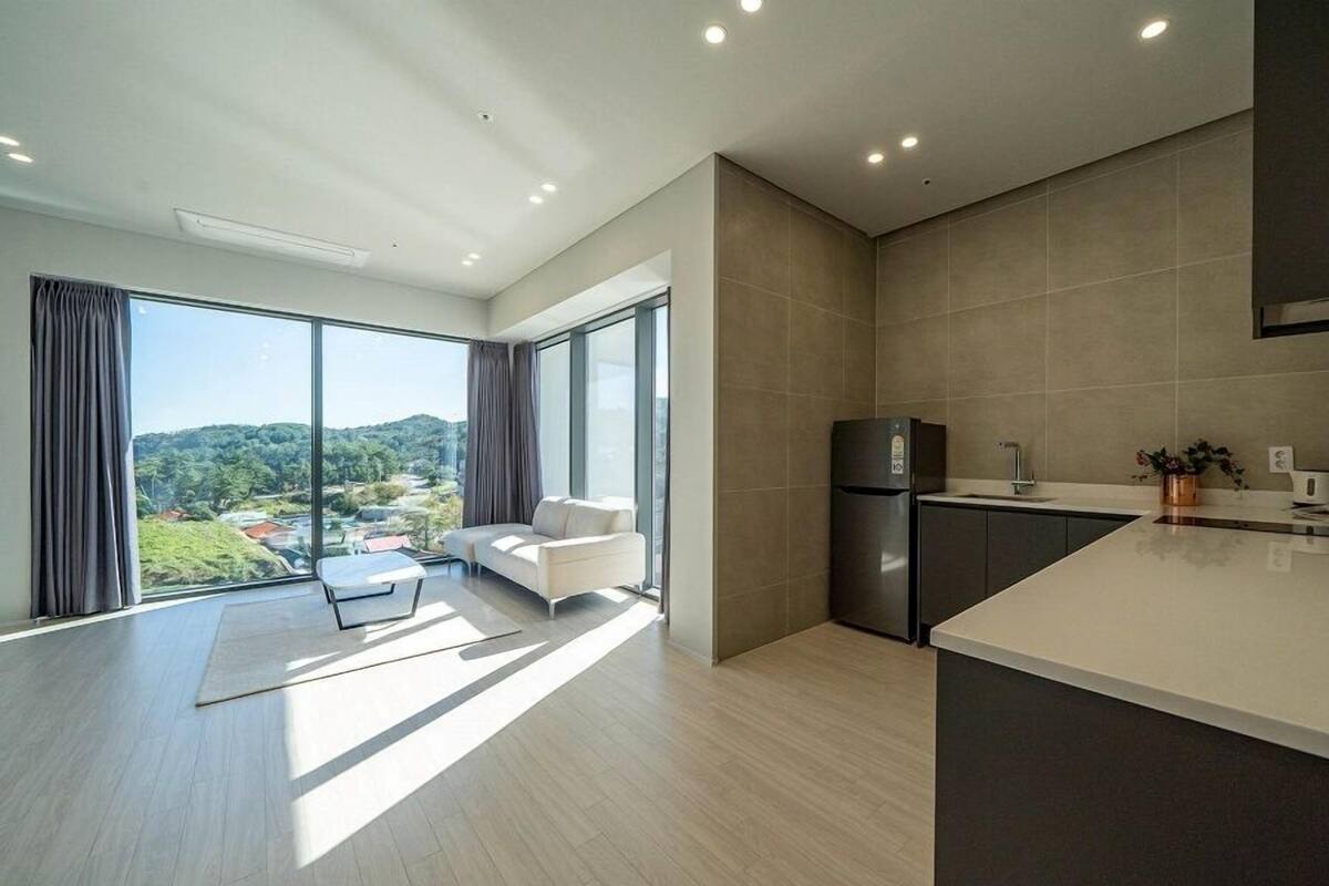 A modern kitchen with a large island, a built-in oven, and a view of a lush landscape through large windows.