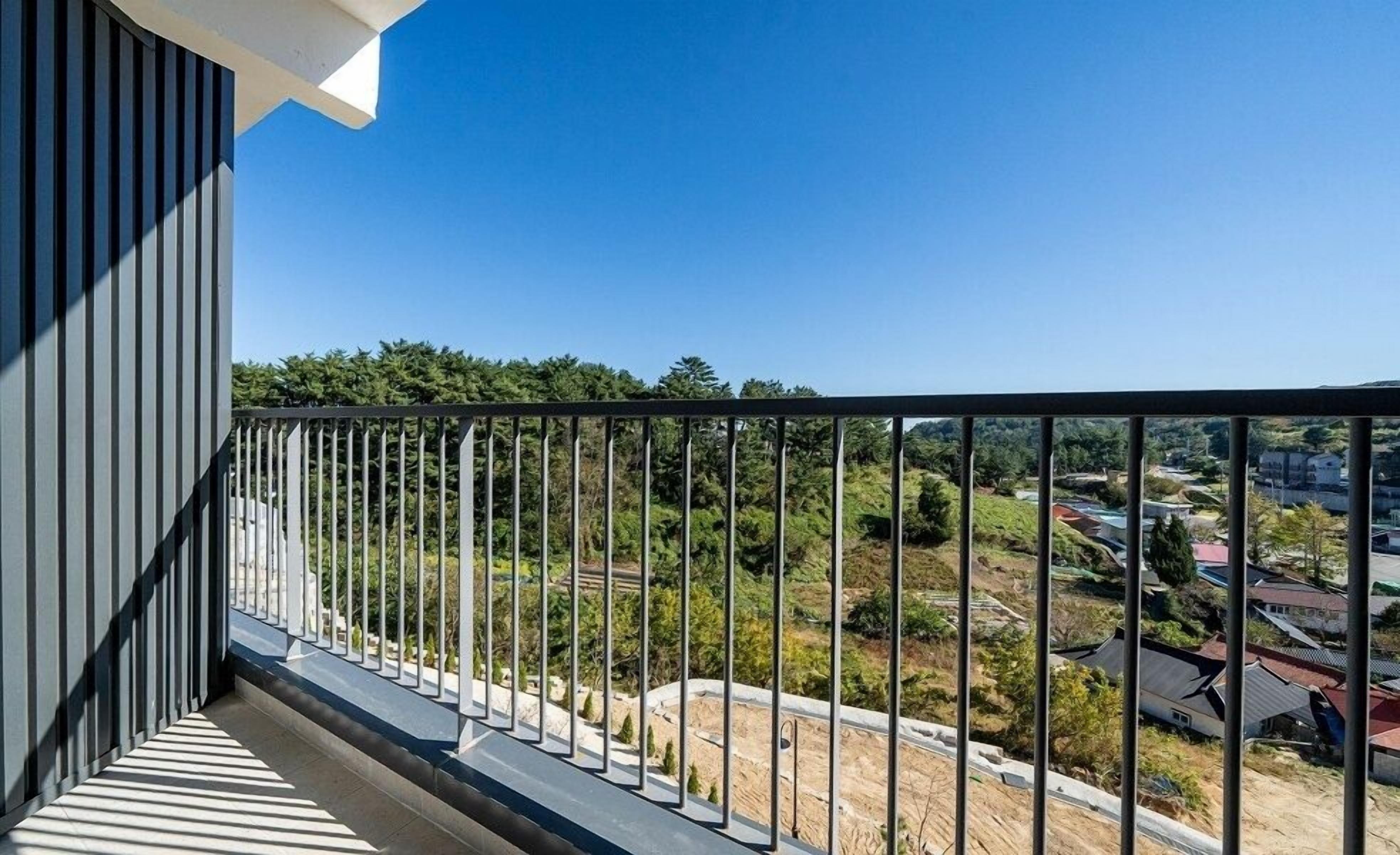 A balcony with a metal railing overlooking a residential area with houses and greenery.