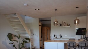Eine moderne Küche mit weißen Schränken, einer zentralen Kochinsel, Barhocker, Pendelleuchten und einer Treppe zu einer oberen Ebene.