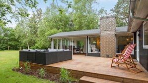A covered outdoor patio with a seating area, a brick fireplace, and a view of the surrounding greenery.