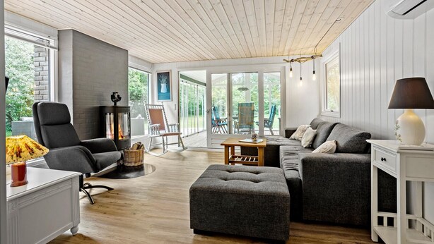 A modern living room with a fireplace, grey furniture, and large windows offering a view of the outdoors.