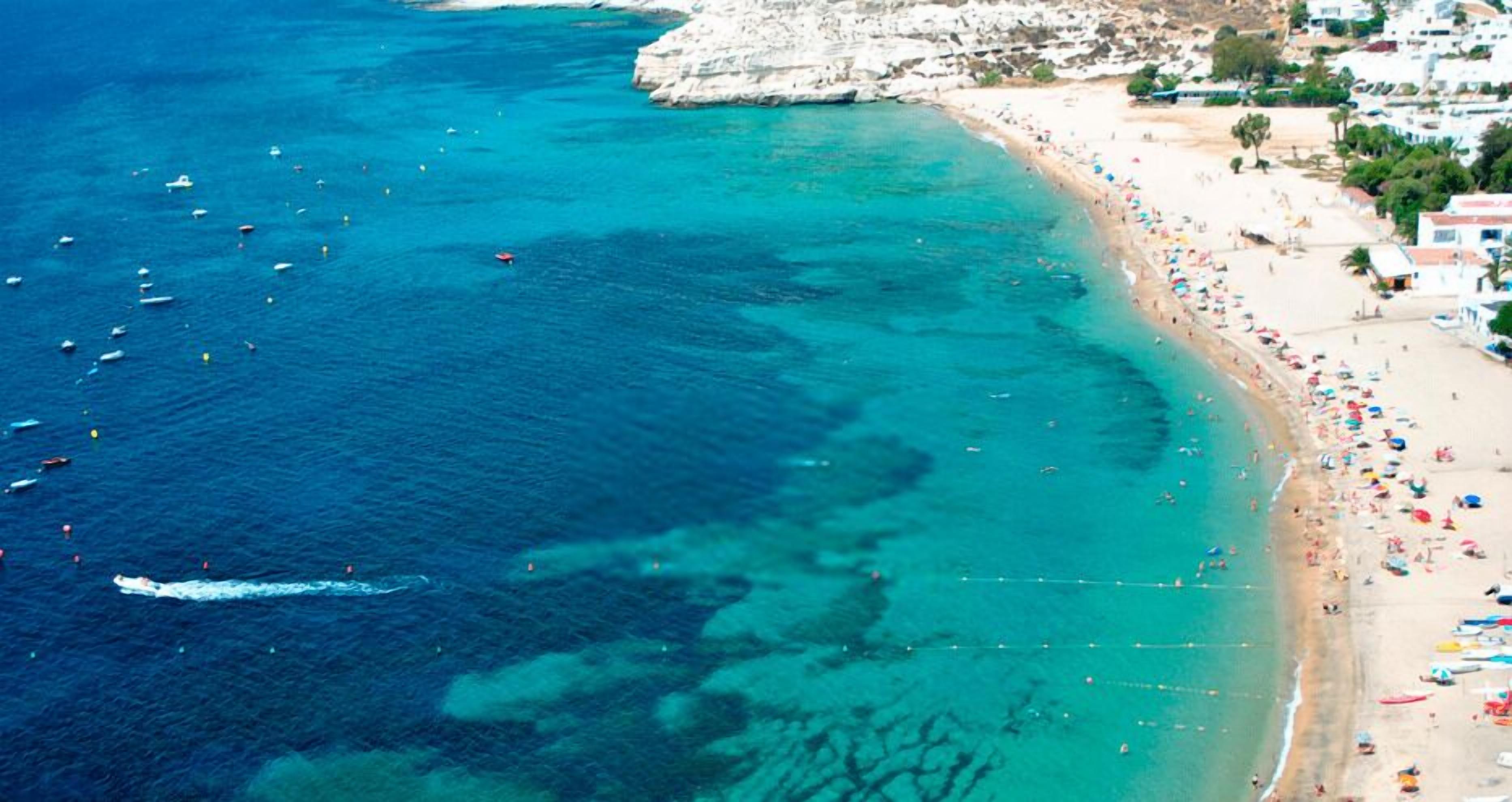 An aerial view of a coastal area with a beach, boats, and buildings.