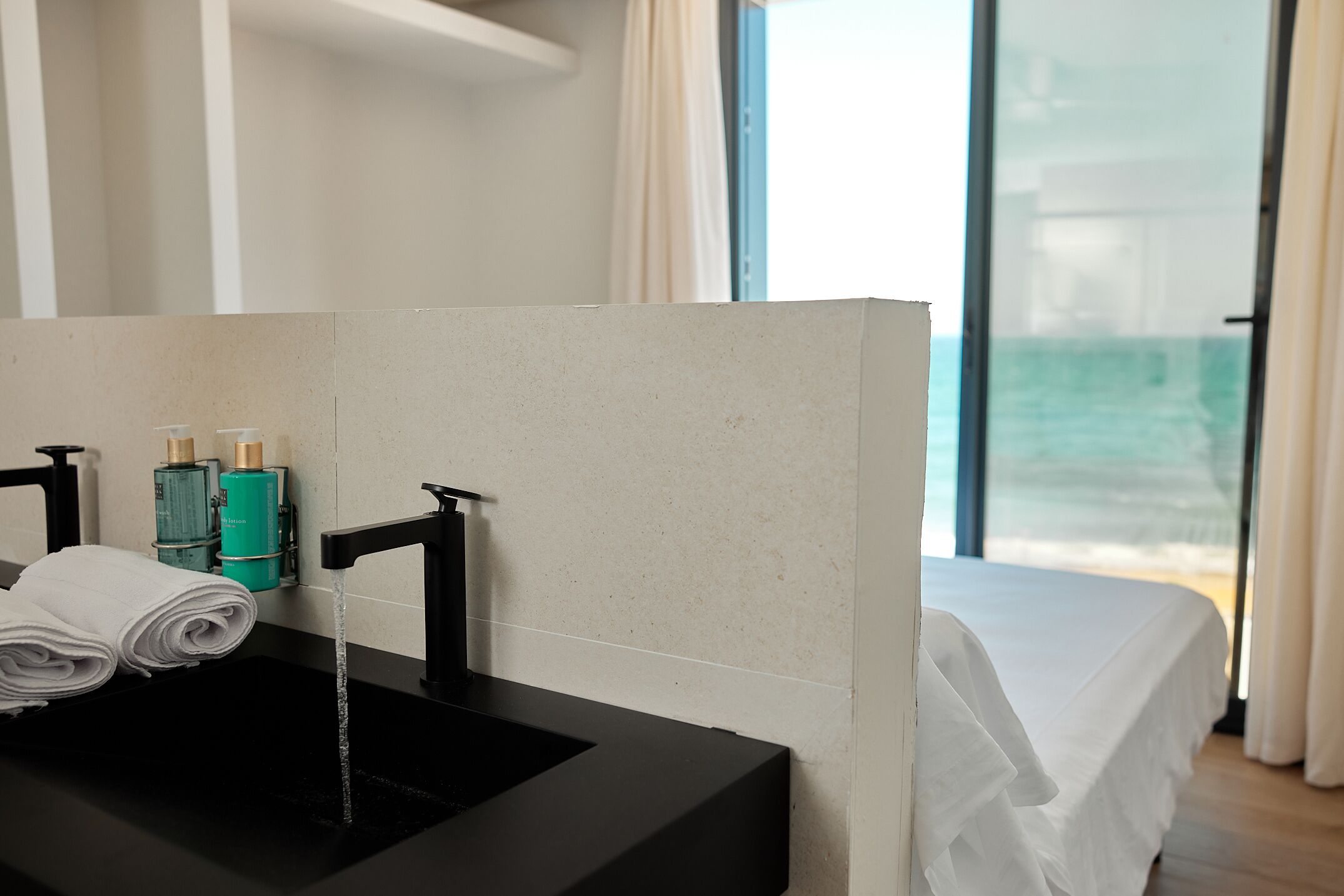 A modern bathroom with a black sink, two toiletries, and a view of the beach through a large window.