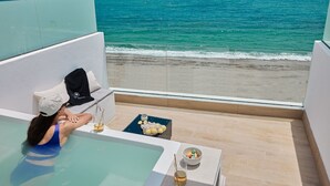 Un balcone con vista sull'oceano, una vasca da bagno e un tavolino con snack e bevande.