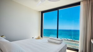 Una camera d'albergo con un grande letto, vista sull'oceano e un balcone con ringhiera.