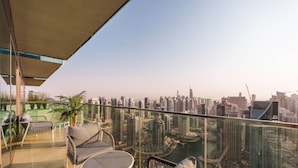 A balcony with a glass railing, outdoor furniture, and a view of a cityscape with high-rise buildings.