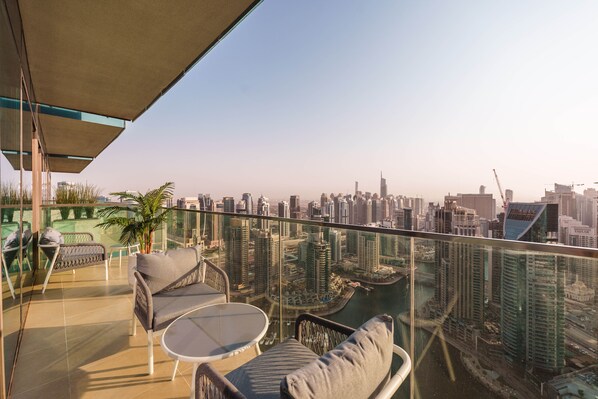 A balcony with a glass railing, outdoor furniture, and a view of a cityscape with high-rise buildings.