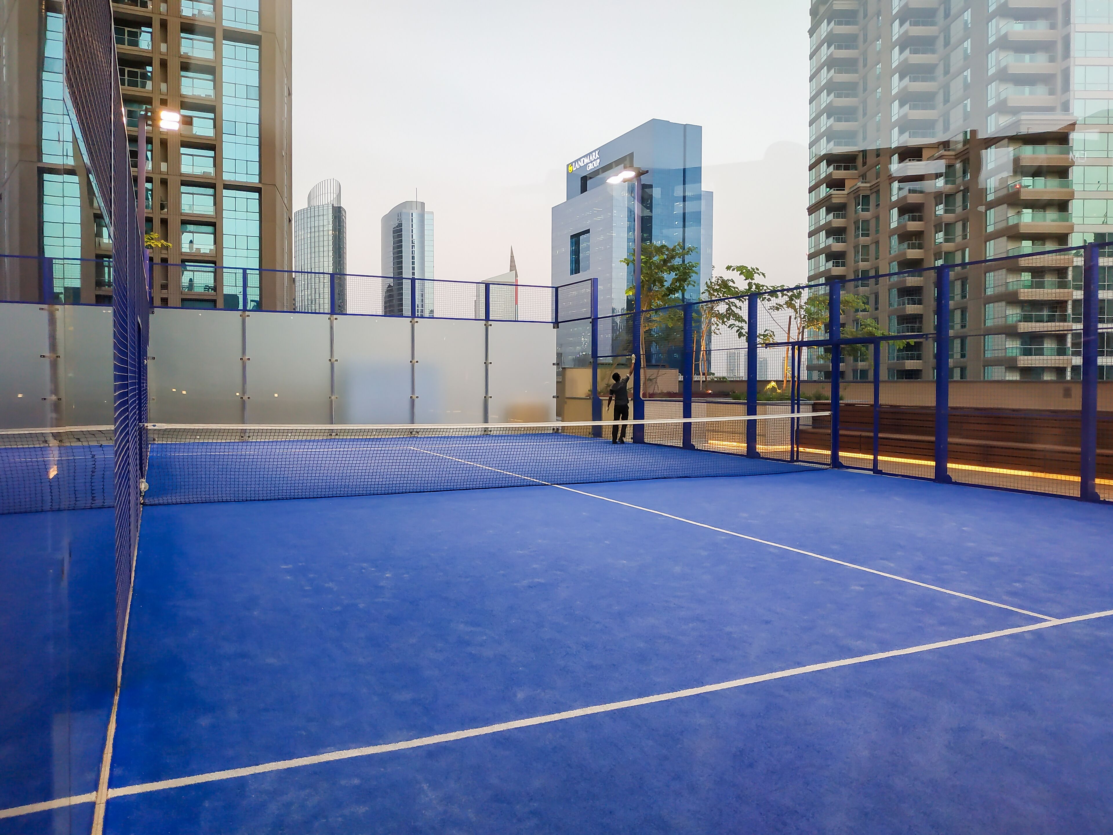 An indoor tennis court with a blue surface, surrounded by high-rise buildings.