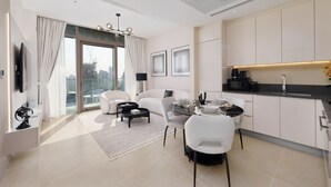 A modern living room with a sofa, coffee table, and dining area. There is a kitchen with a black countertop and white cabinets.