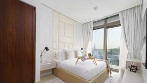 A modern bedroom with a large bed, a nightstand, a bedside table, a window with curtains, and a view of the city.