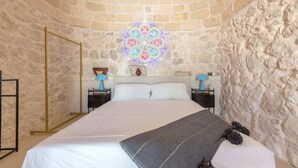 A bedroom with a stone wall, a bed with white linens, a decorative ceiling light, and two bedside tables with lamps. - 3510 Villa Montipuglia by Perle di Puglia (Carovigno)
