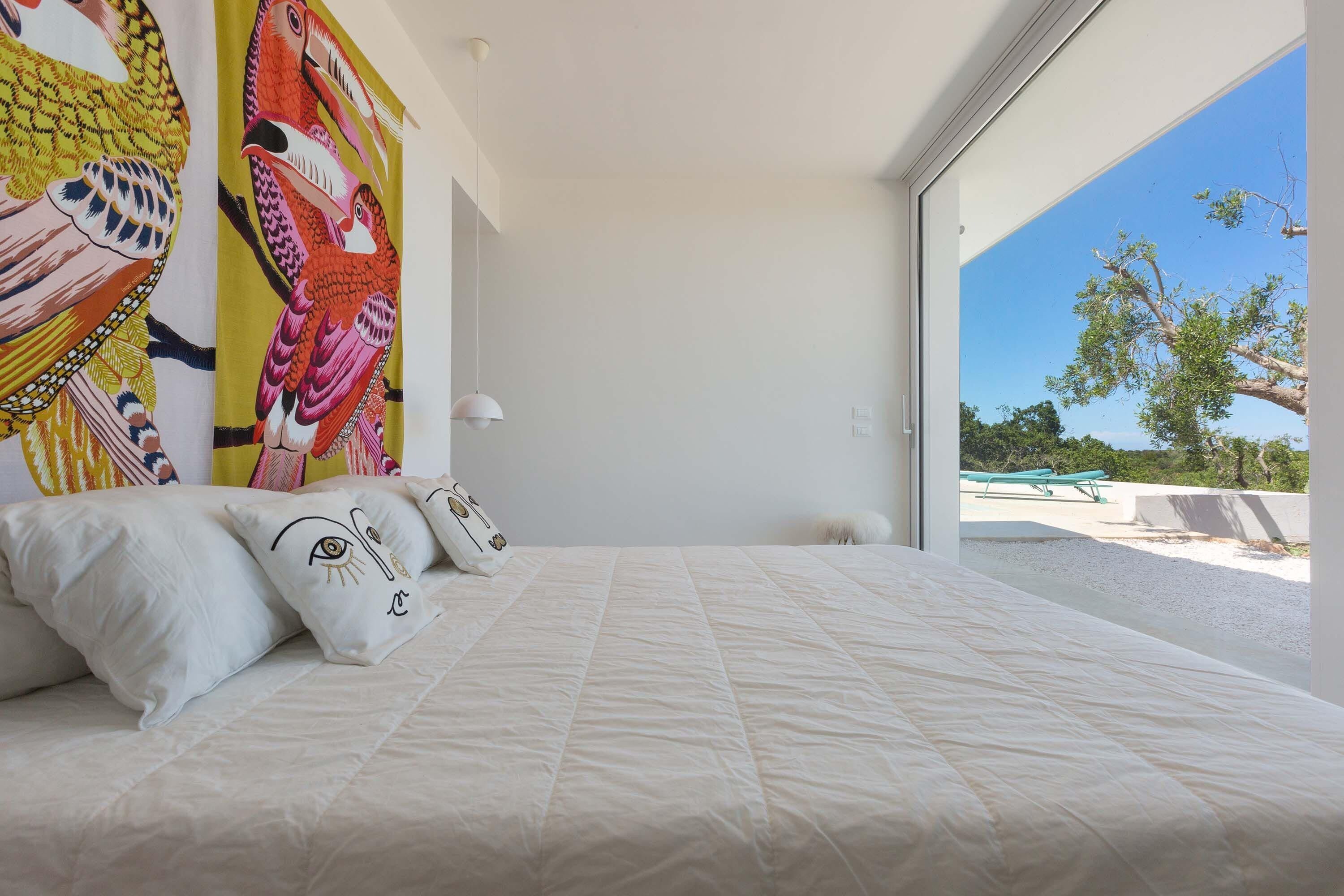 A bedroom with a large bed, a view of the beach, and a colorful mural on the wall.