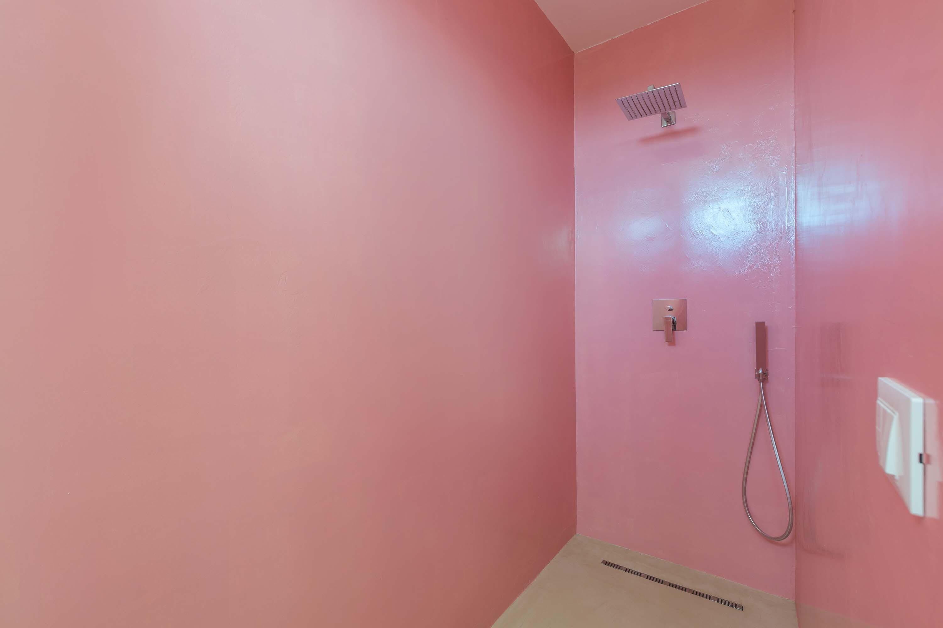 A bathroom with pink walls, a shower, and a toilet.