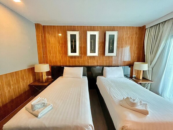 A hotel room with two beds, wooden paneling on the walls, framed pictures above the beds, and lamps on either side.