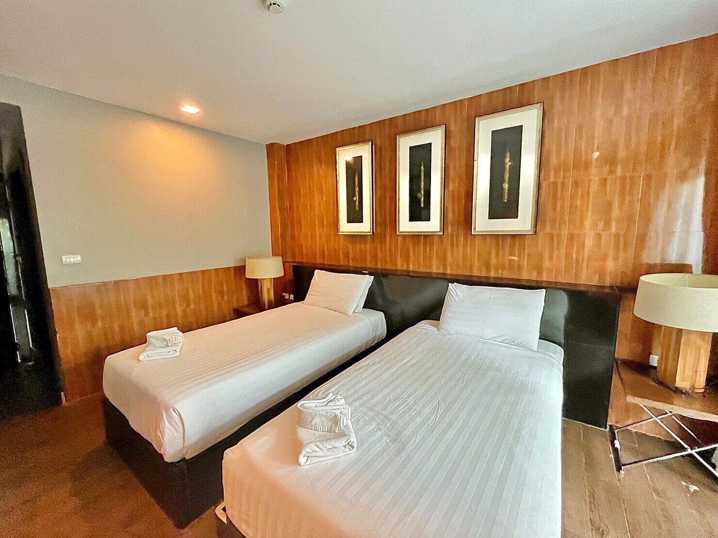 Une chambre d’hôtel avec deux lits simples, des lambris en bois sur les murs et des tableaux encadrés au-dessus des lits.