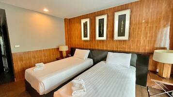 Une chambre d’hôtel avec deux lits simples, des lambris en bois sur les murs et des tableaux encadrés au-dessus des lits.