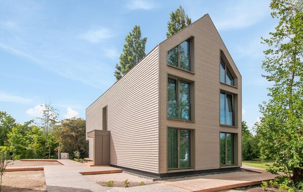 A modern two-story house with a sloped roof, large windows, and a paved patio area.