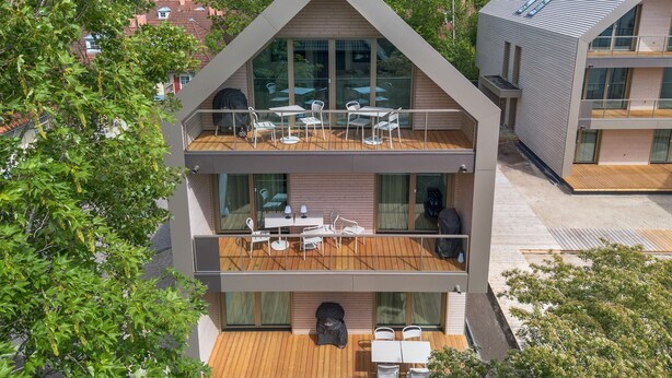 A modern two-story building with a wooden deck, outdoor seating, and large windows.