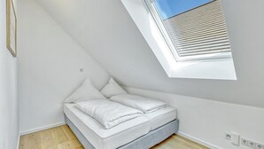 A small, modern bedroom with a sloped ceiling and a skylight.