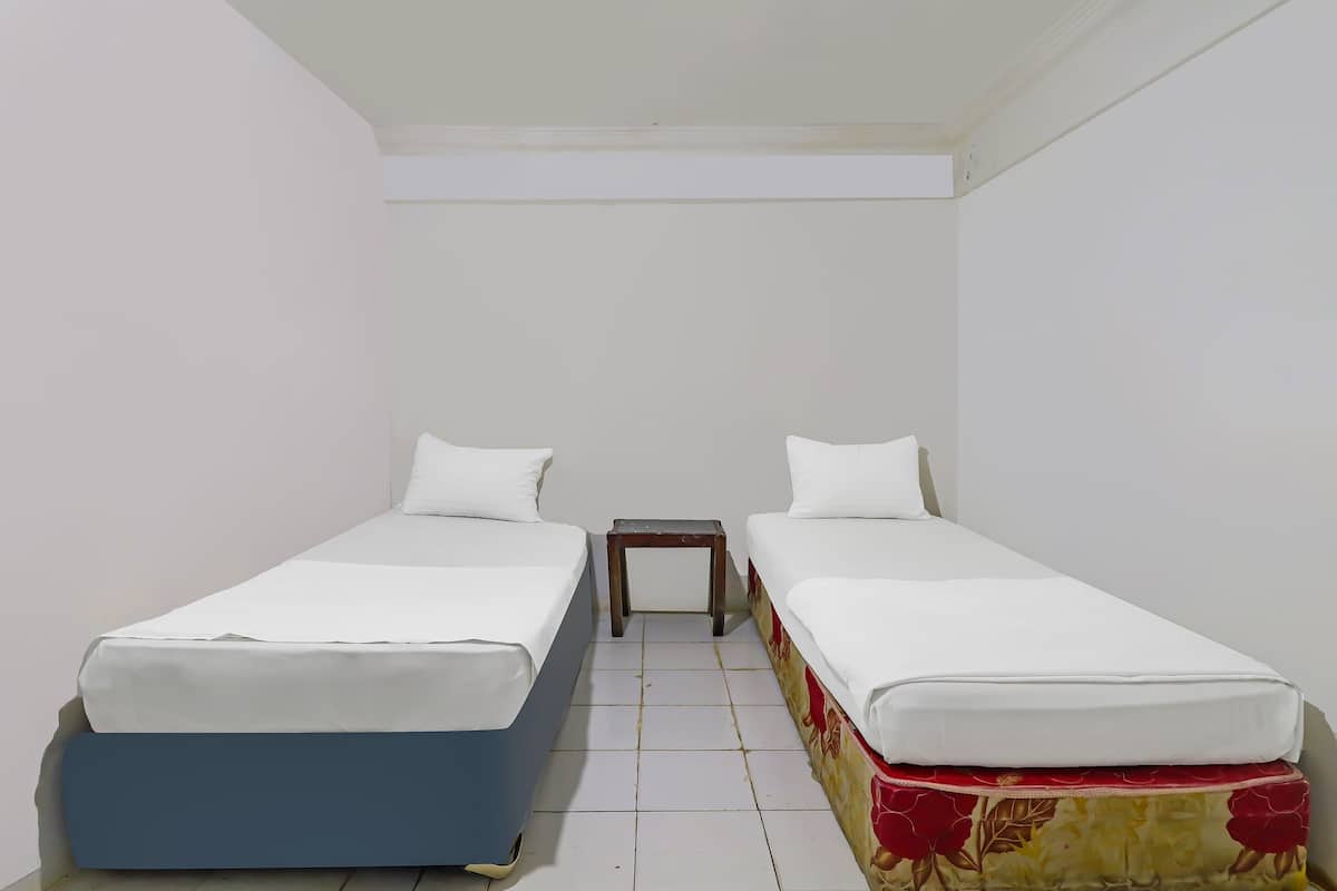 A small, clean room with two single beds, a small wooden nightstand, and white walls.