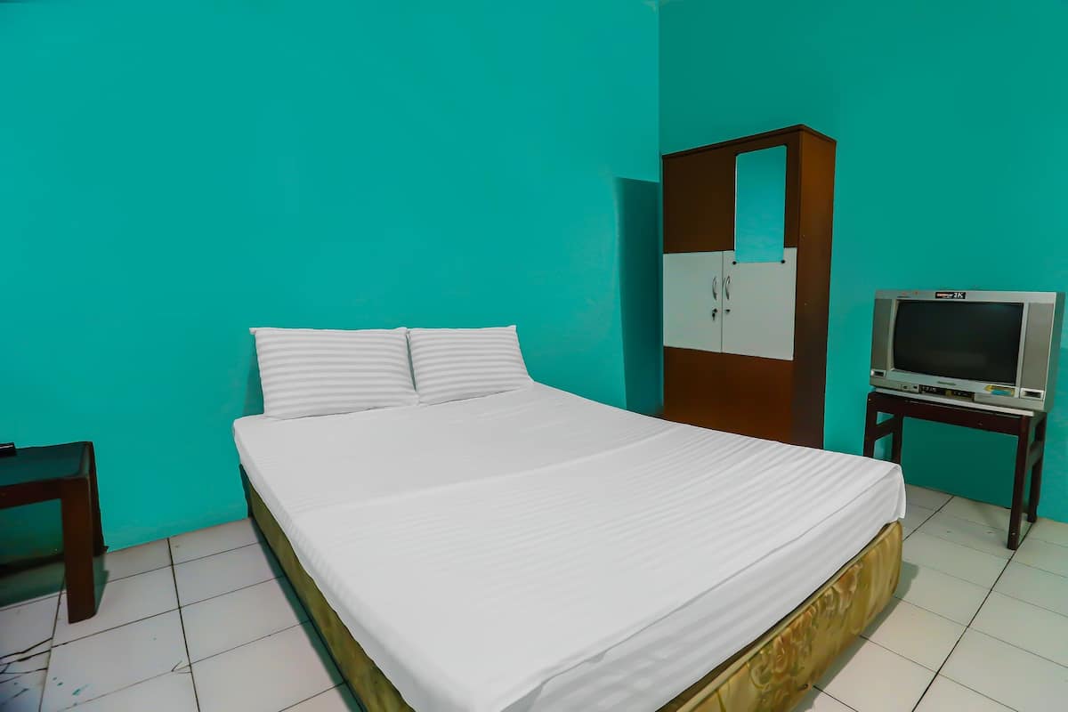 A neatly made bed with white bedding, a wooden wardrobe, and a small table with a television.