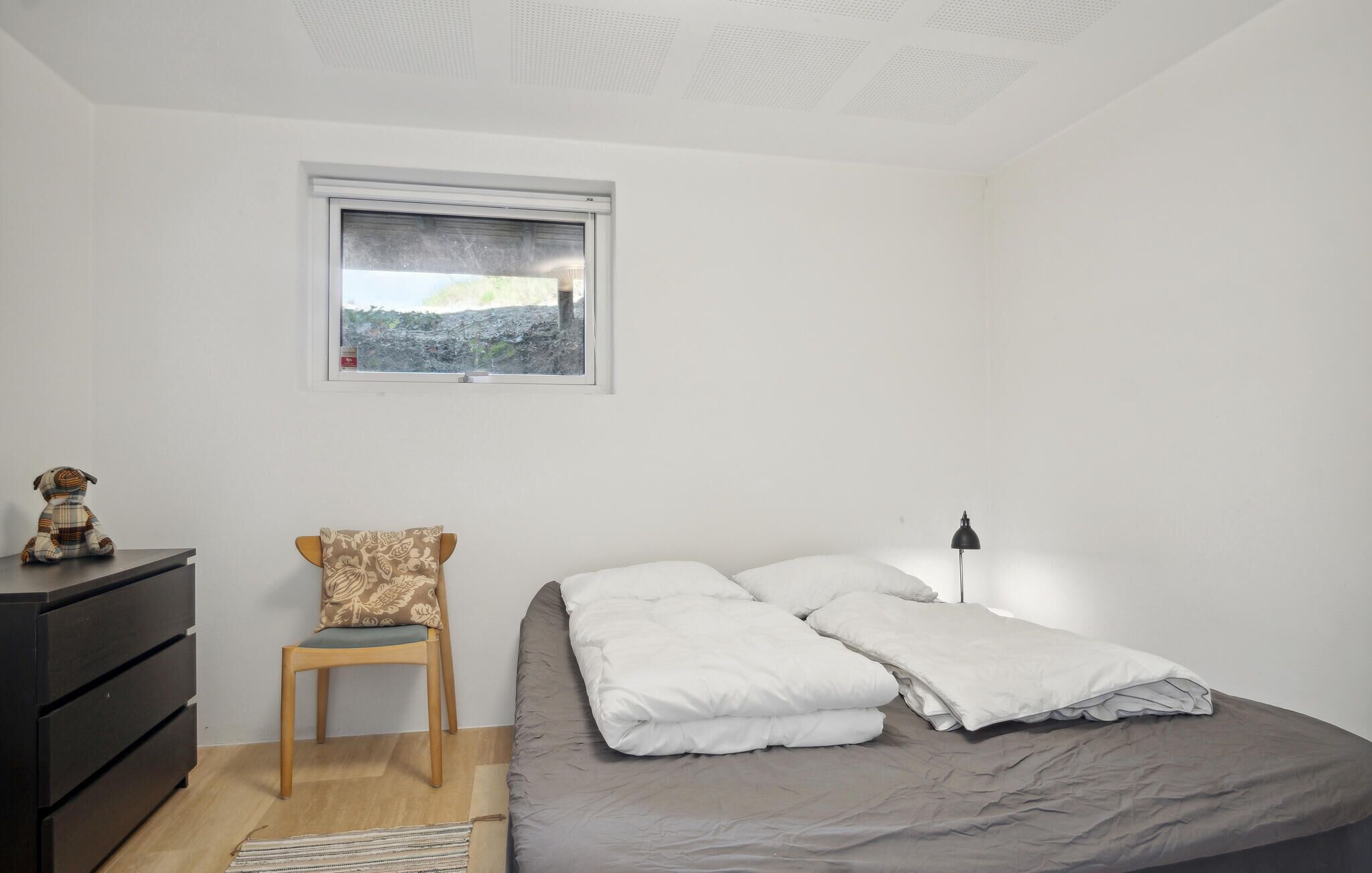 Une chambre à coucher avec un lit, une chaise, une commode, une fenêtre et une lampe.