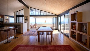 Una cocina amplia con techo de madera, un comedor con una mesa grande y vistas a través de ventanas amplias.