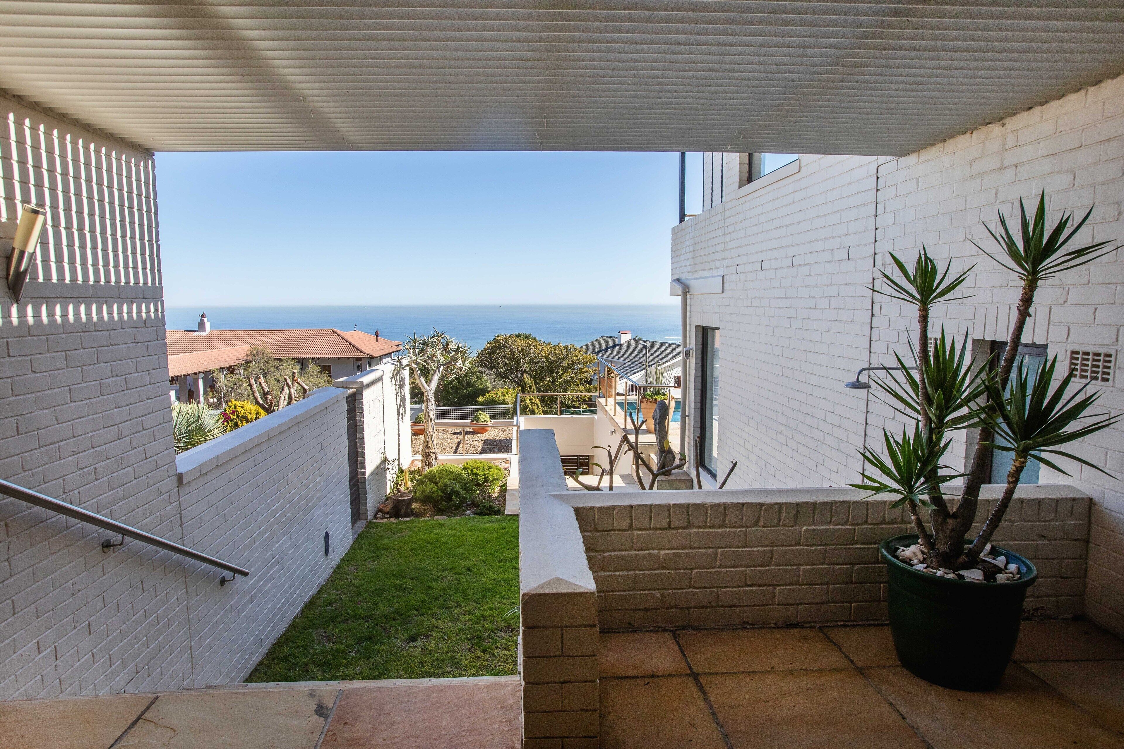 A balcony with a view of the sea, a potted plant, and a white brick wall.