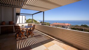 Un balcón con mesa y sillas de madera, una pérgola arriba y vista al mar.