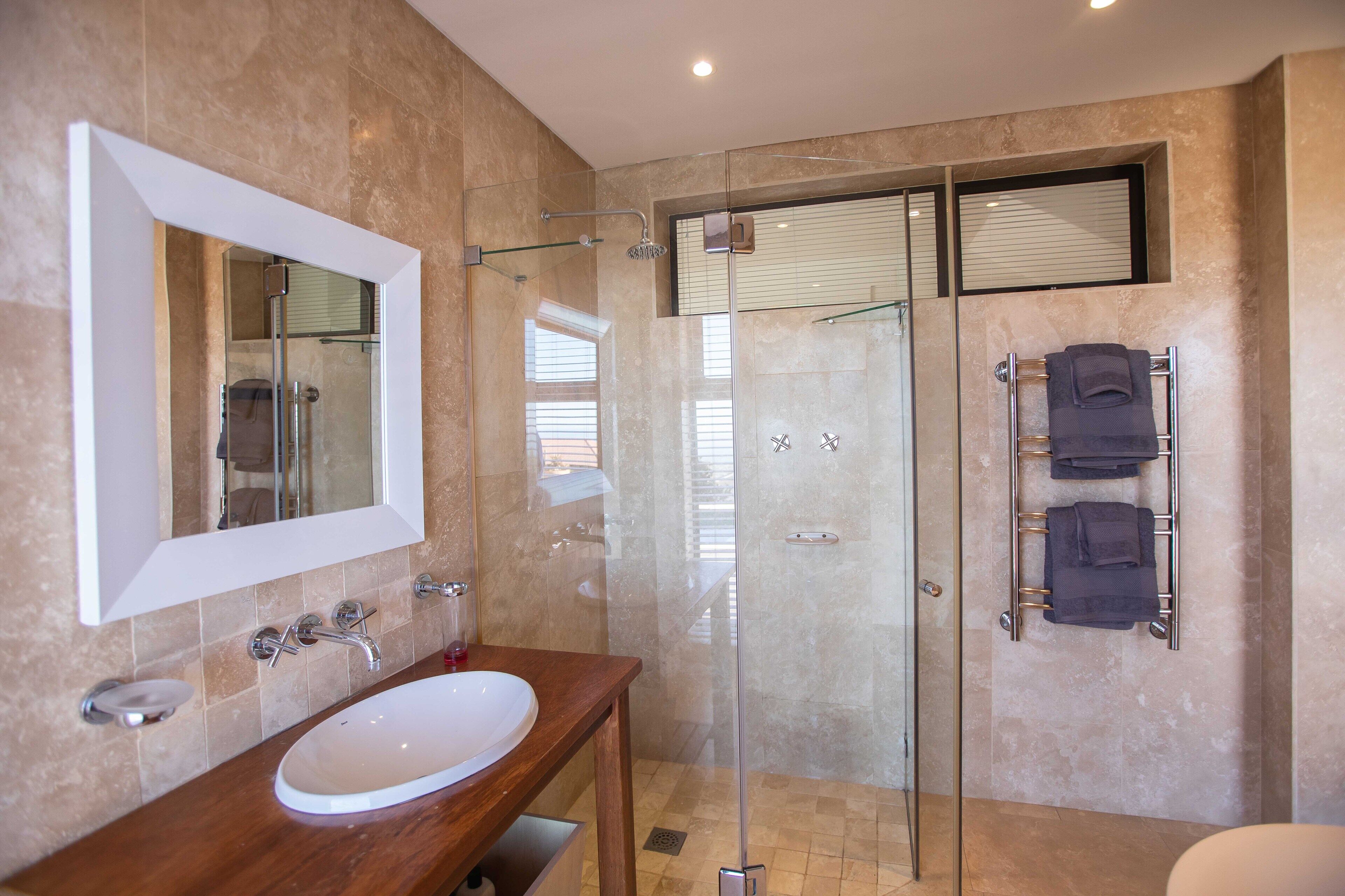 Un baño moderno con ducha acristalada, lavamanos blanco y un perchero para toallas.