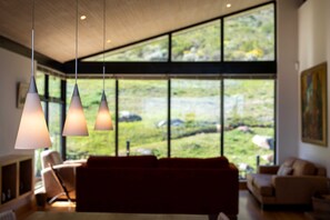 A modern living room with a large window, a sofa, and pendant lights. - Spacious villa on the slopes of Table Mountain with a pool and sea views (Cape Town)