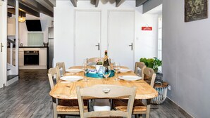 A dining room with a wooden table set for six, surrounded by chairs, and a kitchen visible in the background.