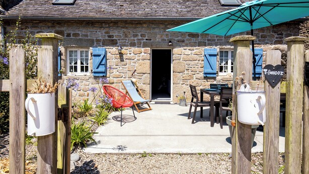 A stone building with a patio area, a wooden gate, and a blue umbrella.