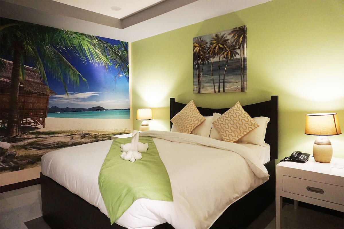 A hotel room with a bed, nightstands, and a wall mural of a beach scene.