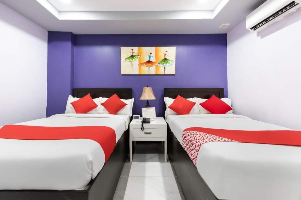A hotel room with two beds, each with red and white bedding, a nightstand with a lamp, and a painting on the wall.