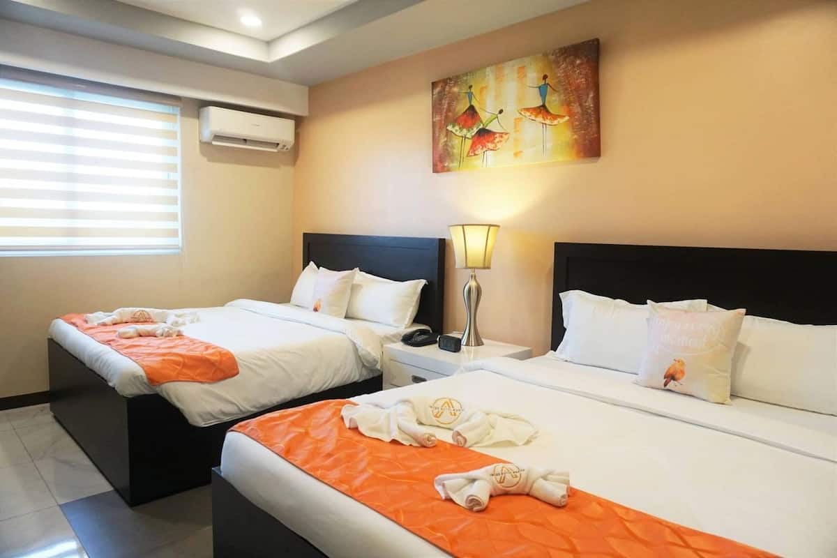 A hotel room with two beds, a painting on the wall, and an air conditioning unit.