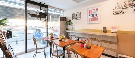 A modern cafe with wooden tables and chairs, a large window, and motivational wall art.