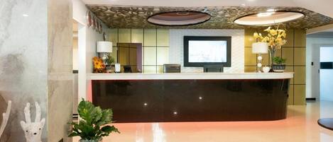 Un área de recepción con un mostrador de mármol, un televisor de pantalla plana y una planta en maceta.