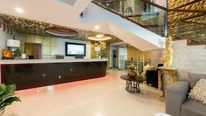 A modern hotel lobby with a reception desk, a staircase, and a seating area.