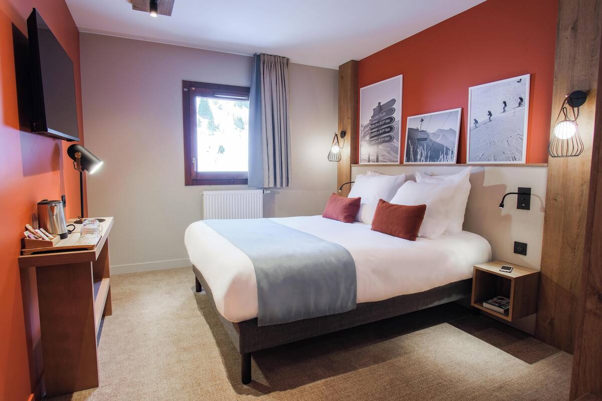 Un dormitorio con cama, mesitas de noche, televisor, obras de arte y una ventana con cortinas.