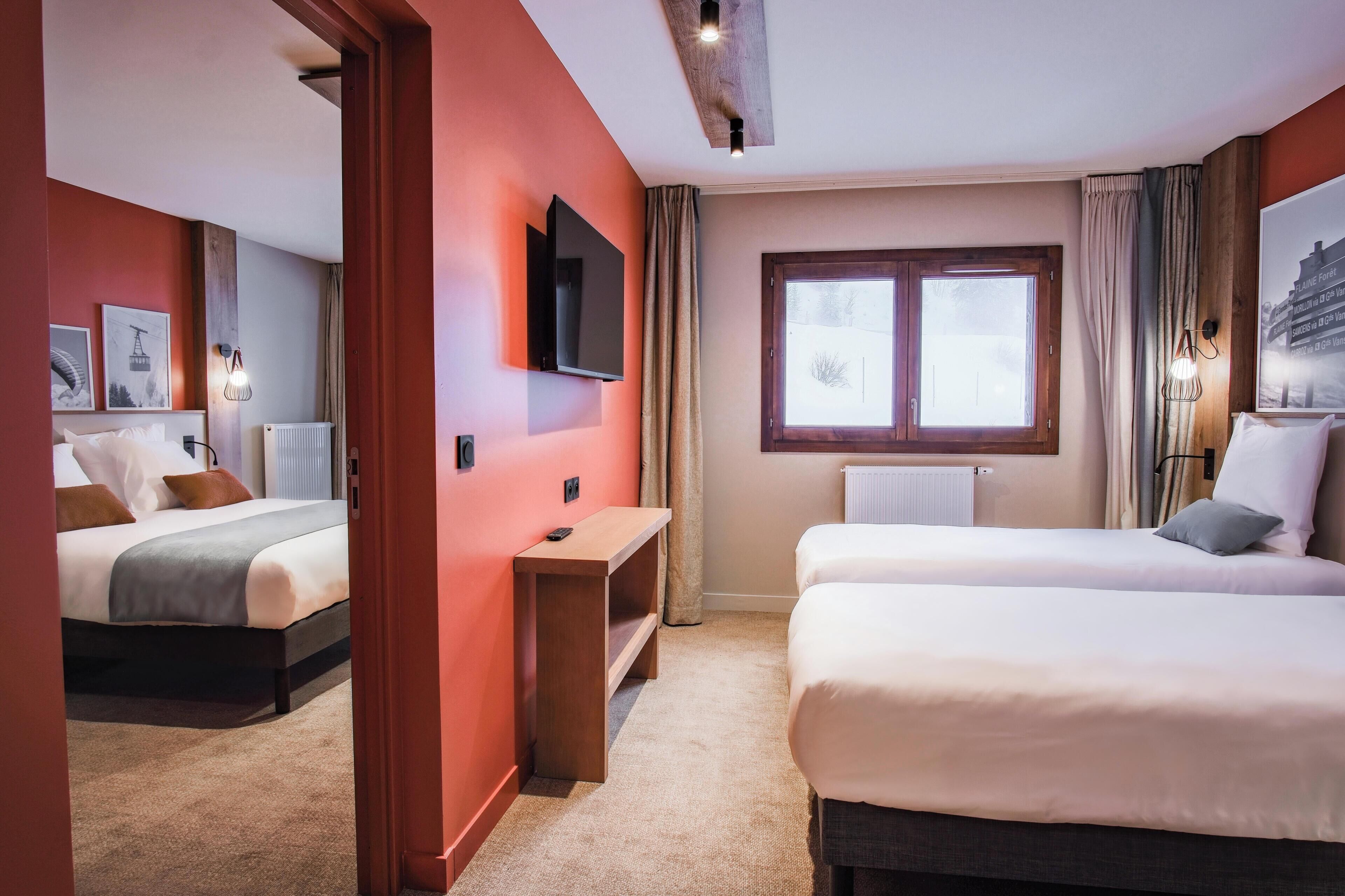 Una habitación de hotel con dos camas, televisión, ventana y una pequeña mesa.