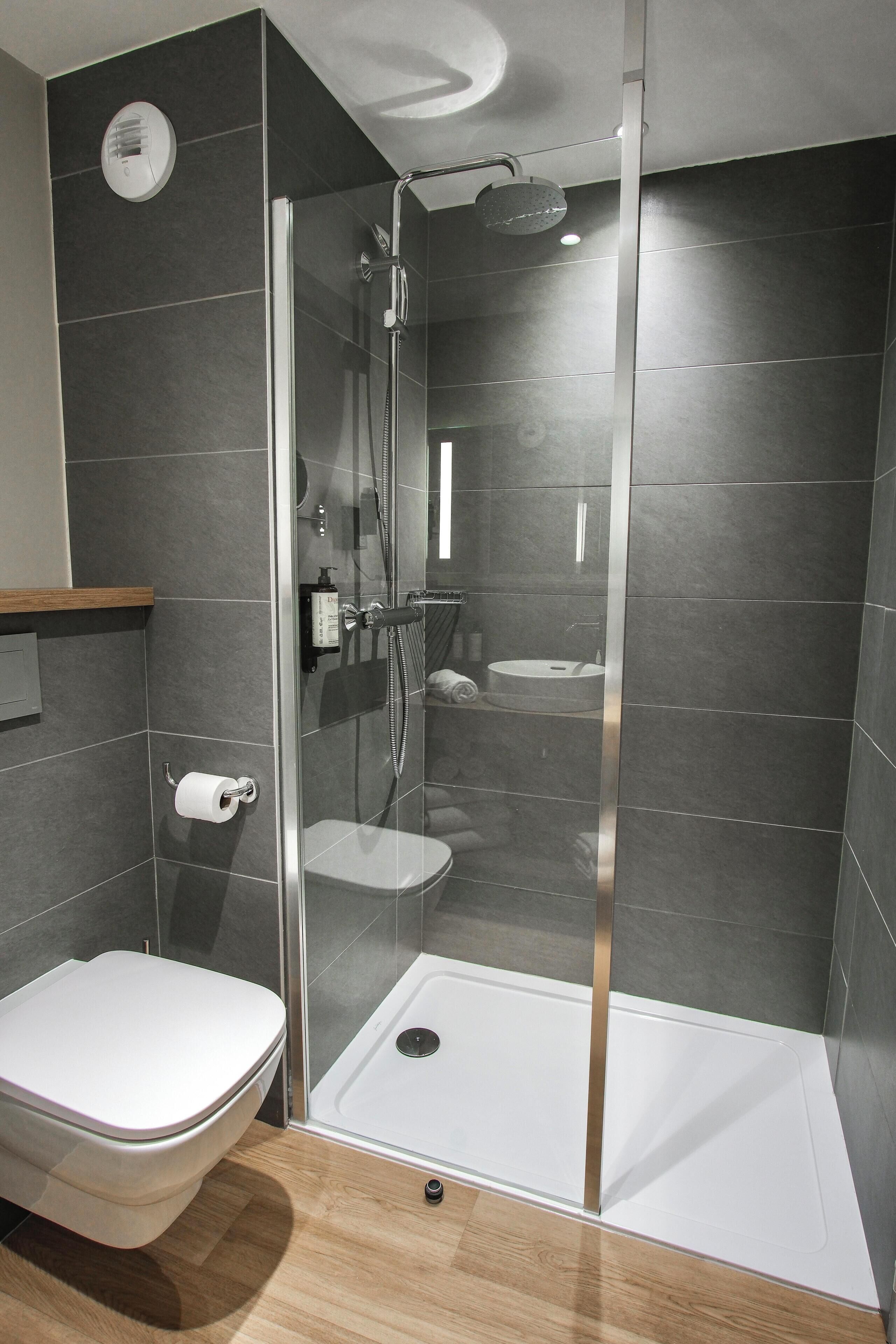 A modern bathroom with a glass-enclosed shower, a toilet, and a sink.