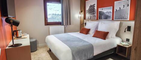 Una habitación de hotel moderna con una cama grande, una cafetera, una mesita de noche y una ventana con vistas a un paisaje nevado.