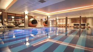 Una piscina interior moderna amb un disseny de sòl geomètric, zones d'estar amb seients i grans columnes decoratives.