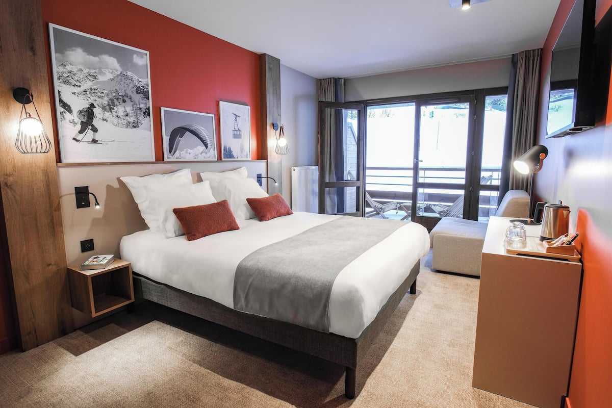 Una habitación de hotel moderna con una cama grande, un escritorio y vistas al exterior a través de un amplio ventanal.