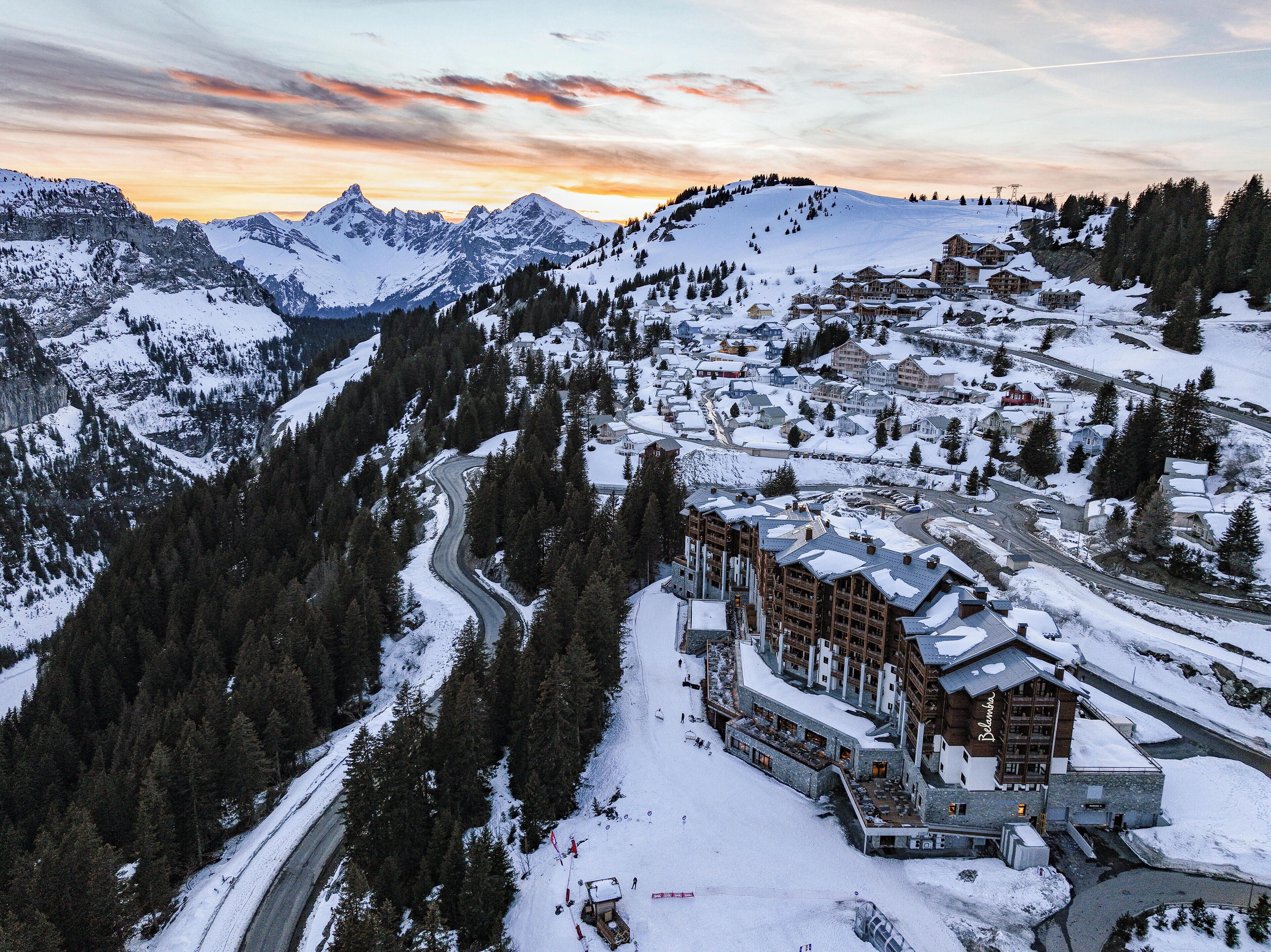 Un resort en la montaña cubierto de nieve, con un camino sinuoso, edificios y una destacada cabaña con un letrero que dice "Belambra".