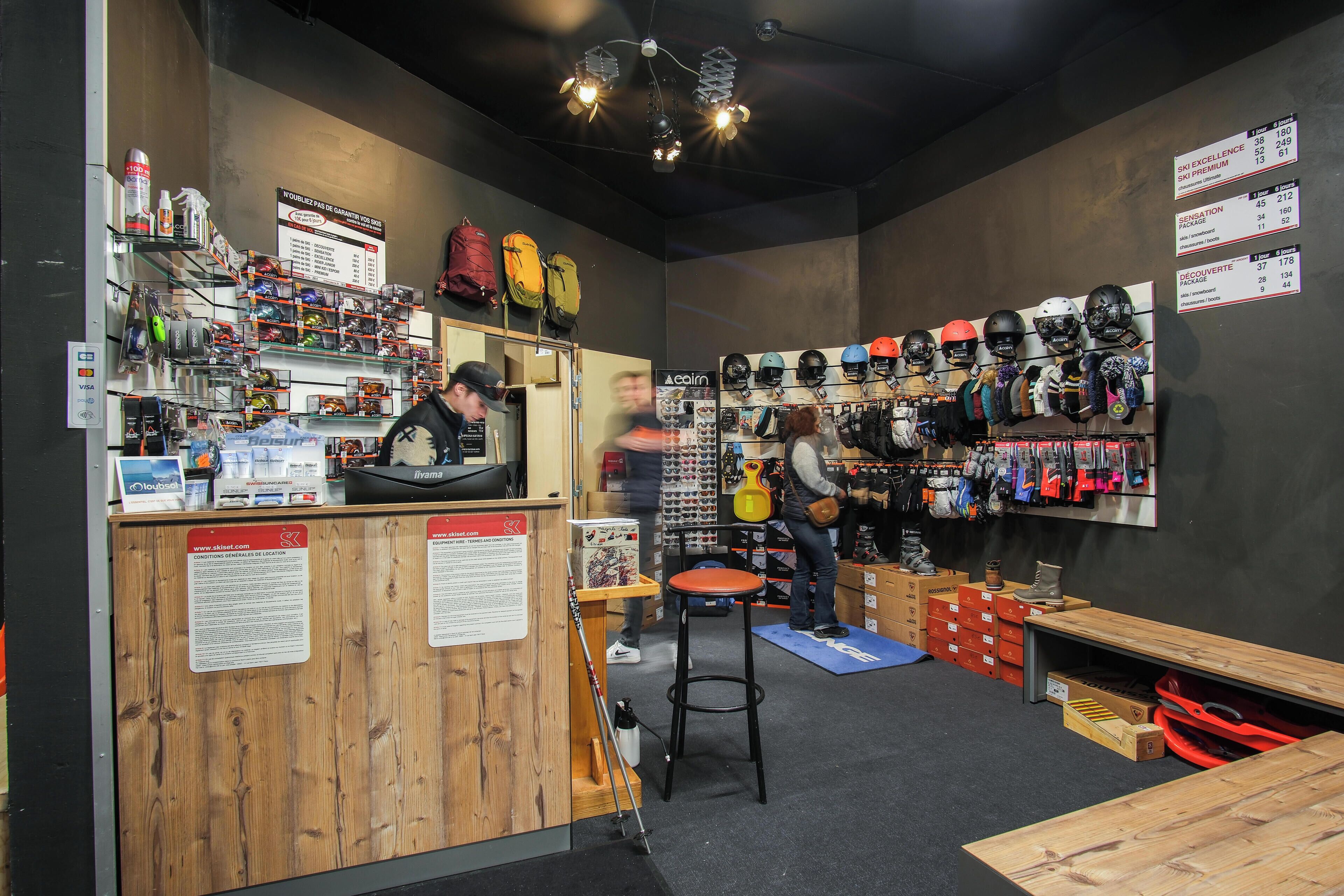 A store with shelves of helmets, a counter with a person behind it, and another person working at a table.
